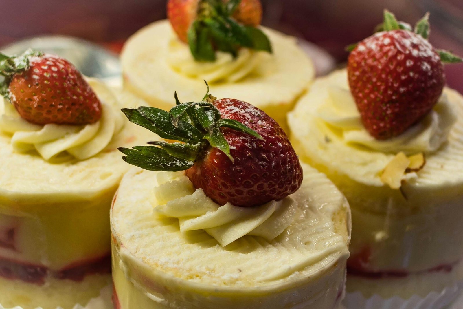 Close-up view of creamy mini cakes topped with fresh strawberries, perfect for indulgent dessert lovers.